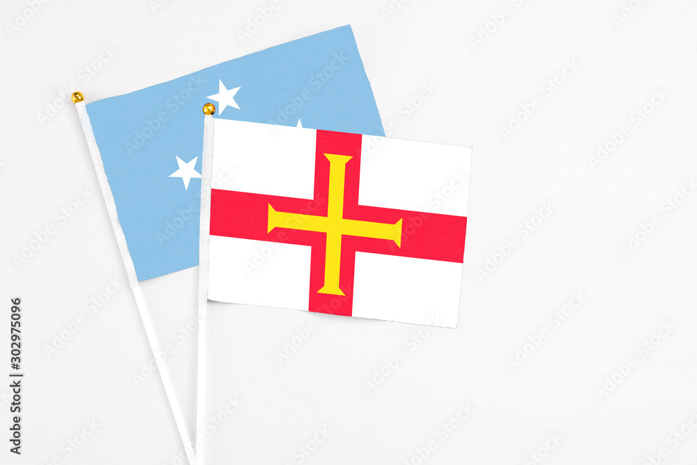 Guernsey and Micronesia stick flags on white background. High quality fabric, miniature national flag. Peaceful global concept.White floor for copy space.