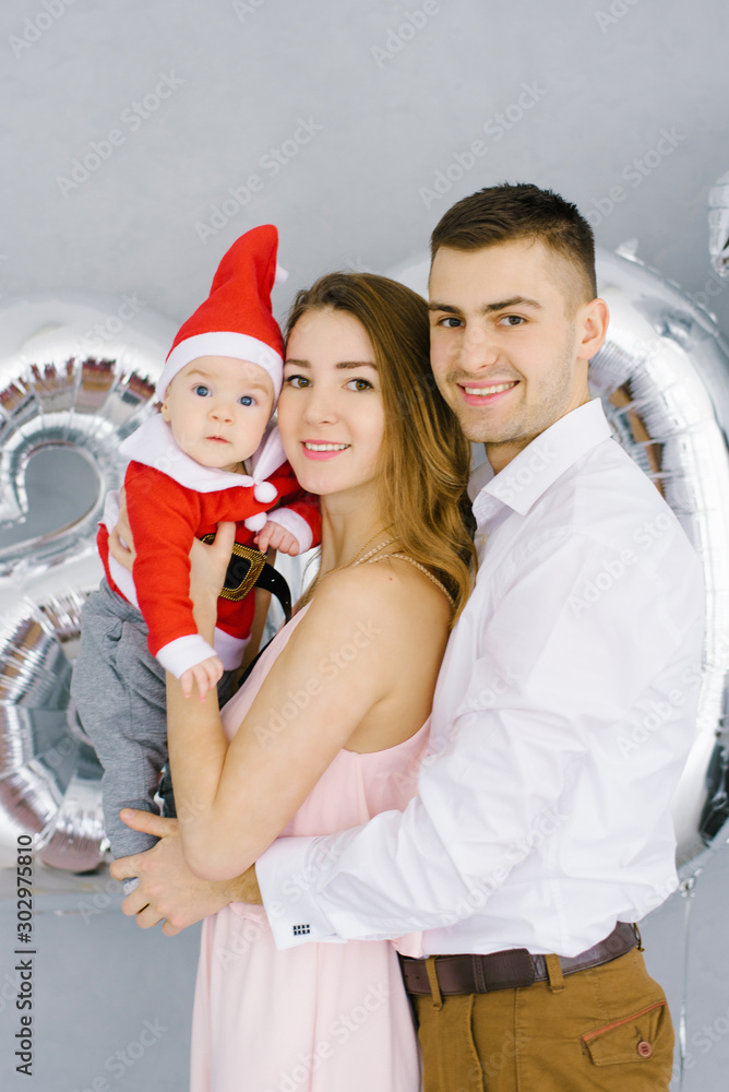 Obraz premium Happy beautiful young family with baby in little Santa costume smile and celebrate new year 2020