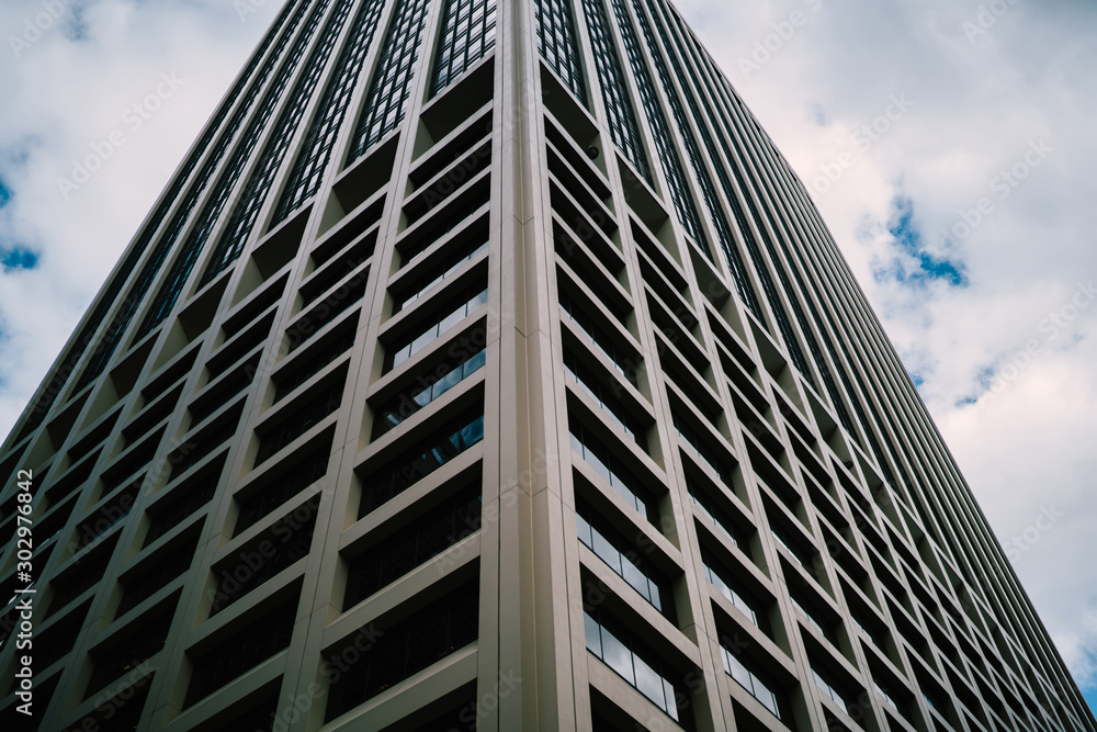 Perspective view of tall concrete skyscraper with windows on exterior rising up in sky, geometric corporate building with offices and luxury apartments for rent in business center of megalopolis.