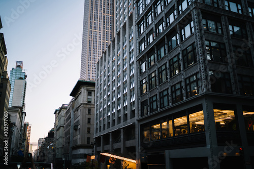 Evening view of tall building exterior with real estate for commercial and residential rent in midtown, urban architecture with high skyscrapers and old construction fronts on street in New York