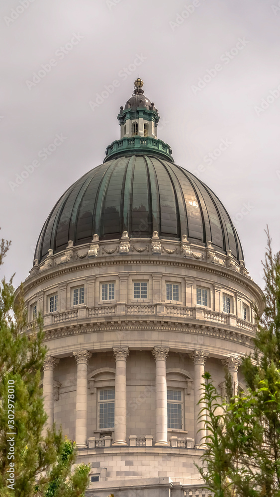 Fototapeta premium Vertical frame Famous Utah State Capitol Building dome framed with trees against cloudy sky