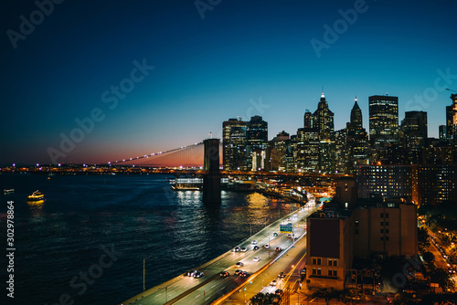 Evening view of financial district of megalopolis with modern architecture near river, New York cityscape with developed infrastructure with skyscrapers bridges and rush traffic on highway in downtown