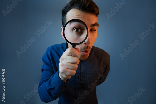 Curious young man with magnifying glass Isolated on grey background. photo