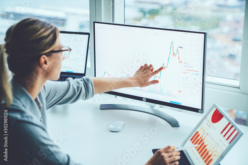 Business woman study financial market to calculate possible risks and profits.Female economist accounting money with statistics graphs pointing on screen of computer at desktop. Quotations on exchange photo