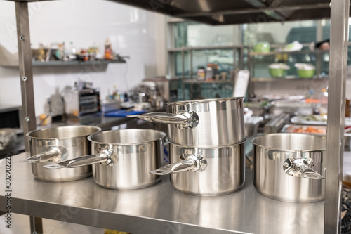 kitchen pots, grater, bowls, saucepans stacked up on a shelf in a kitchen; restaurant / commercial or home kitchen. Brick wall in the background Stock photo