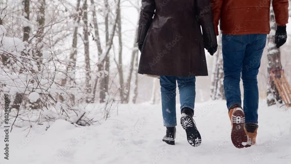 Back view of loving couple feet walking in a park on snowfall. Man and ...