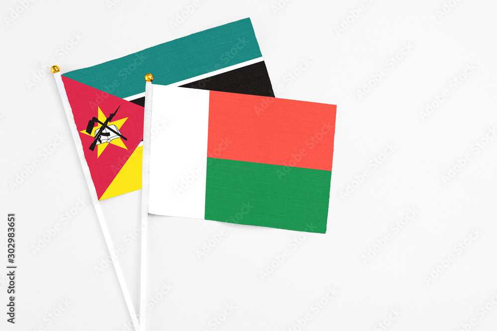 Fototapeta premium Madagascar and Mozambique stick flags on white background. High quality fabric, miniature national flag. Peaceful global concept.White floor for copy space.