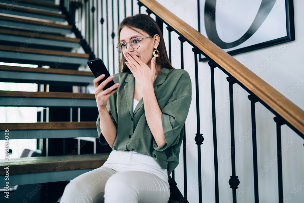 Shocked female having break on stairs and browsing cellphone