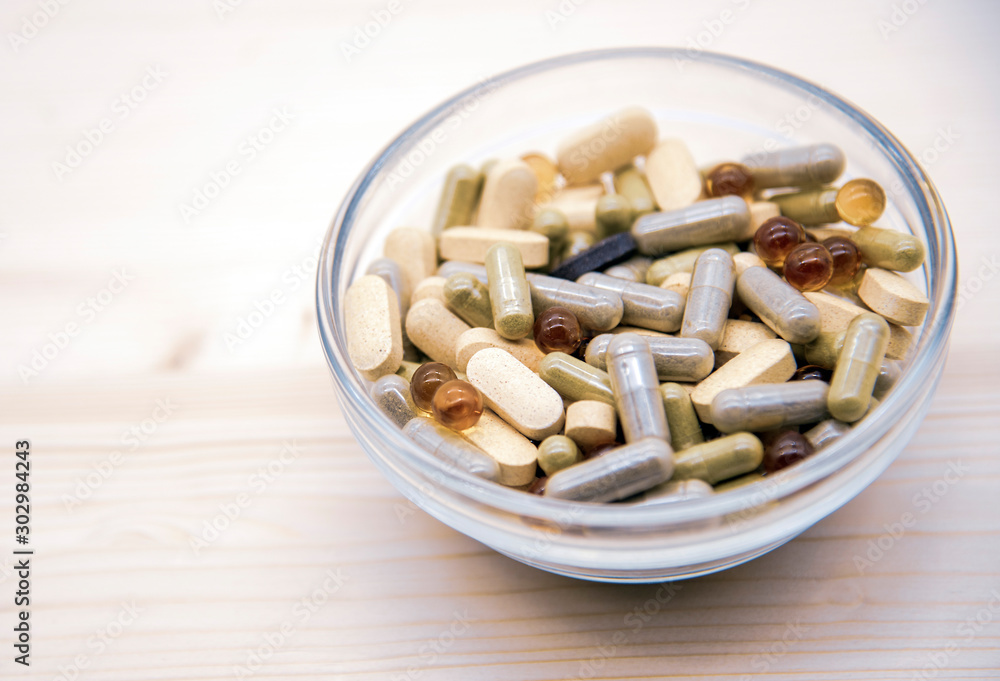 Glass bowl with lots of pills and capsules on a wooden background. Glass bowl with lots of pills and capsules on a wooden background.