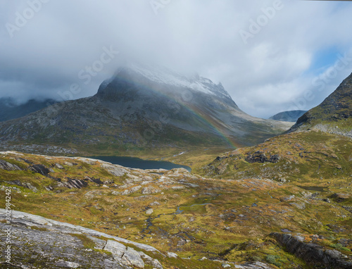 Lake Alnesvatnet with snow capped mountain peak and rainbow. View from scenic road 63 in the Reinheim national Park near the popular road Trollstigen, Norway