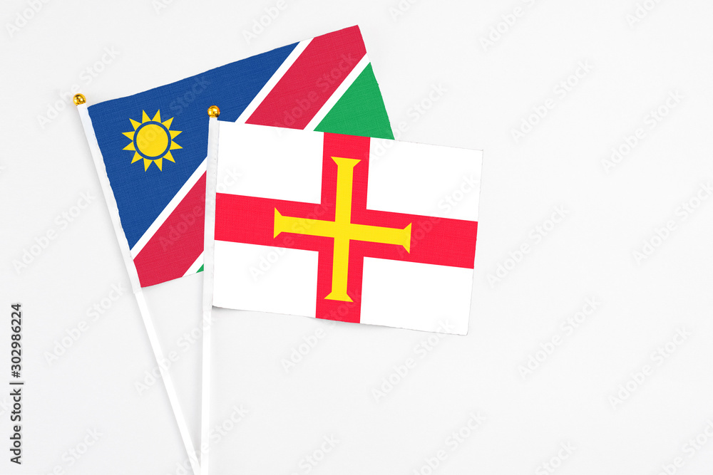 Fototapeta premium Guernsey and Namibia stick flags on white background. High quality fabric, miniature national flag. Peaceful global concept.White floor for copy space.