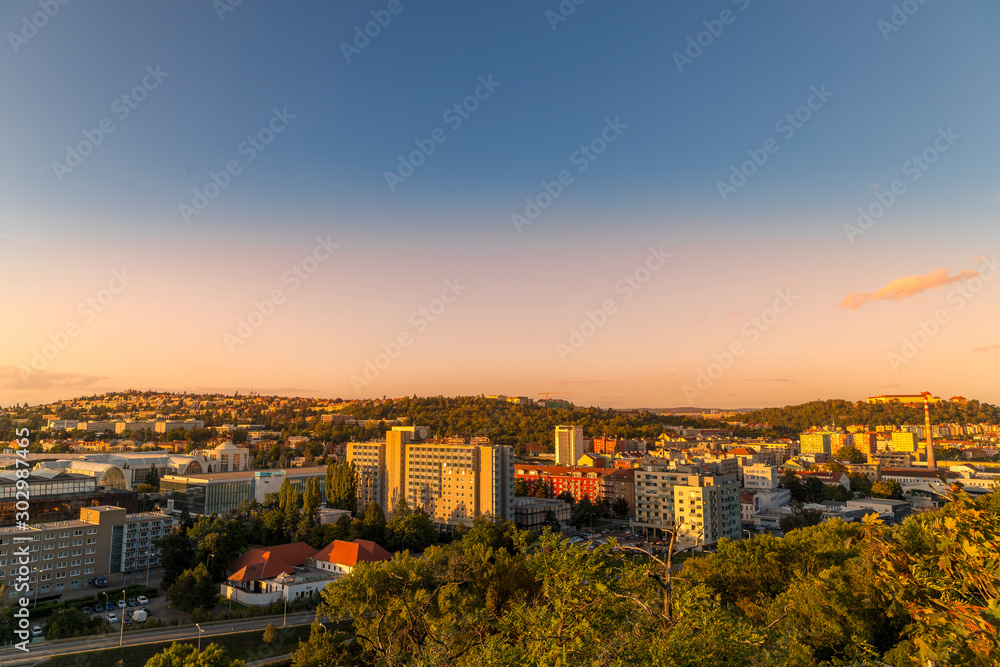 Sunset on Brno city part with exhibition center and apartments on a hill during orange sunset and public light turning online