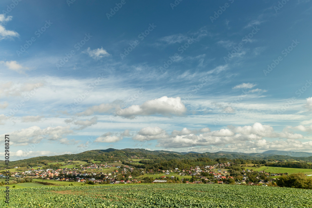 Fast moving clouds in the sky captured during a sunny day overlooking the village and the high hills and mountains in the background foreground from a field with freshly sown crops.