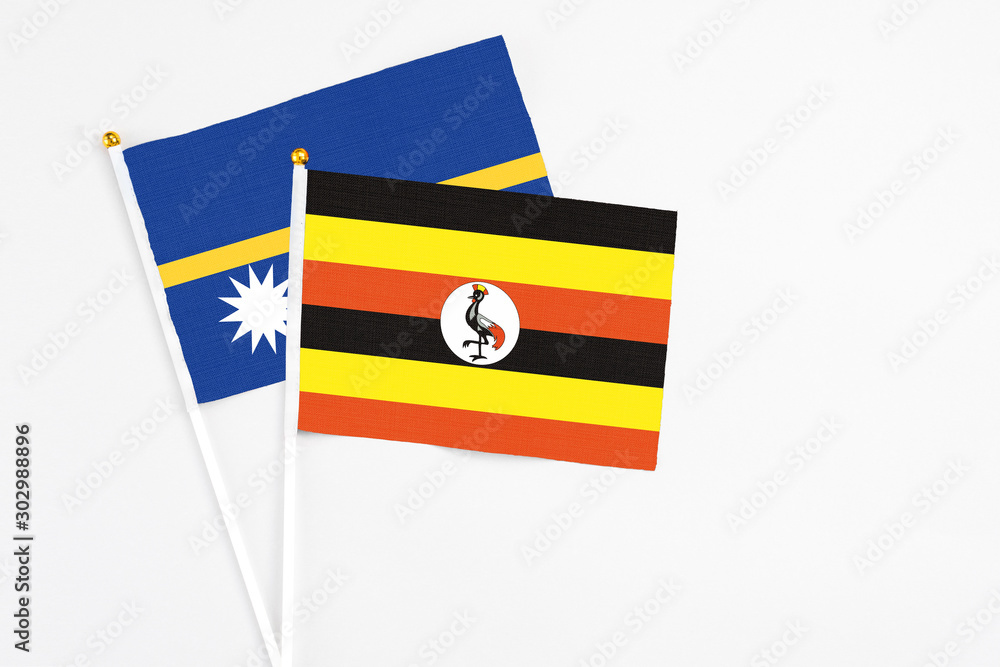 Fototapeta premium Uganda and Nauru stick flags on white background. High quality fabric, miniature national flag. Peaceful global concept.White floor for copy space.