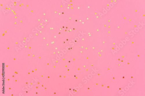 Photo of gold color stars glitter sprinkles on pink trendy background. Festive holiday background for your projects. Celebration concept. Christmas pattern. Top view, flat lay