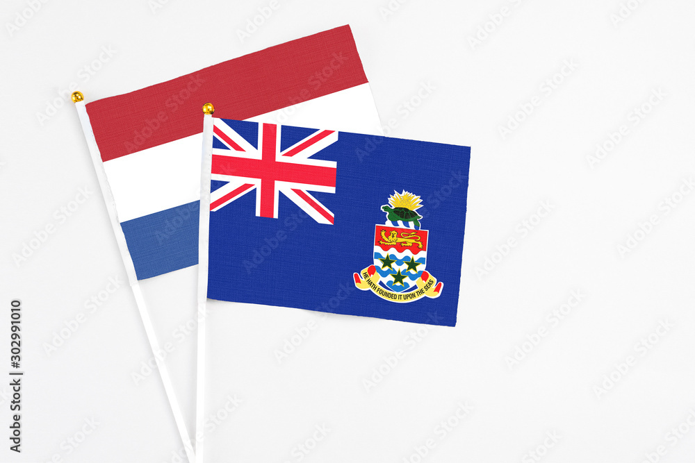 Fototapeta premium Cayman Islands and Netherlands stick flags on white background. High quality fabric, miniature national flag. Peaceful global concept.White floor for copy space.