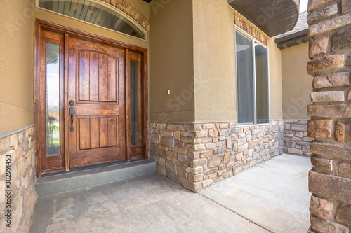 Home porch and brown wood front door with sidelights and arched transom window