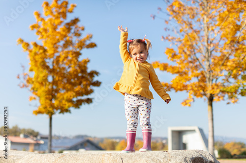 Toddler girl standing on the rock between two yellow trees