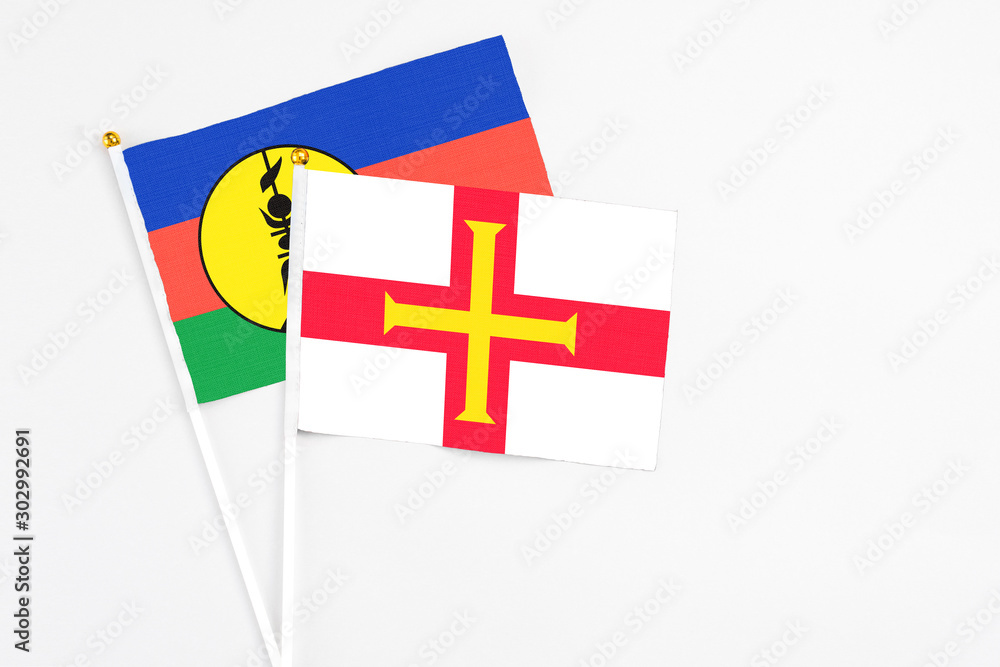 Guernsey and New Caledonia stick flags on white background. High quality fabric, miniature national flag. Peaceful global concept.White floor for copy space.
