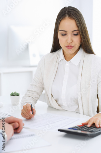 Business woman and man sitting and working with computer and calculator in office. Bookkeeper or accountant checking balance or making finance report. Tax and audit concepts