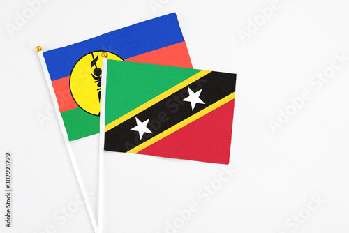 Saint Kitts And Nevis and New Caledonia stick flags on white background. High quality fabric, miniature national flag. Peaceful global concept.White floor for copy space. photo