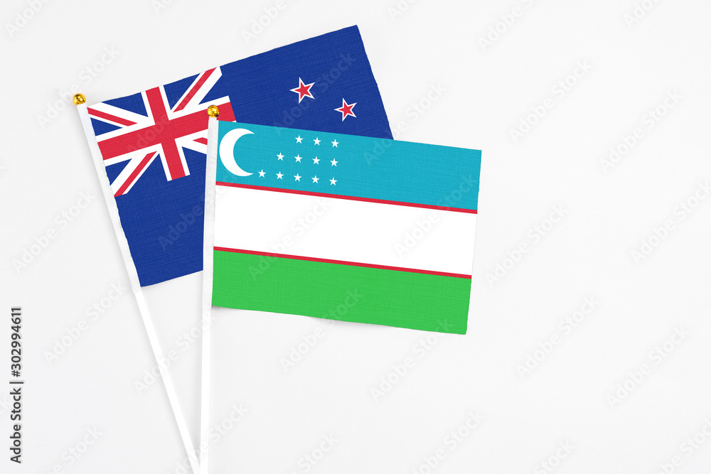 Naklejka premium Uzbekistan and New Zealand stick flags on white background. High quality fabric, miniature national flag. Peaceful global concept.White floor for copy space.