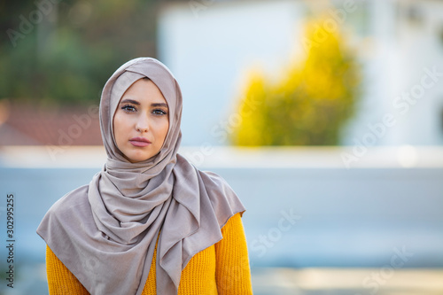 Portrait of young muslim woman wearing hijab head scarf in city while looking at camera. Closeup face of cheerful woman covered with headscarf smiling outdoor. Casual islamic girl at park. photo