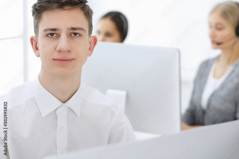 Call center. Group of operators at work. Focus at young guy receptionist in headset at customer service white colored office. Business concept Call center. Group of operators at work. Focus at young guy receptionist in headset at customer service white colored office. Business concept