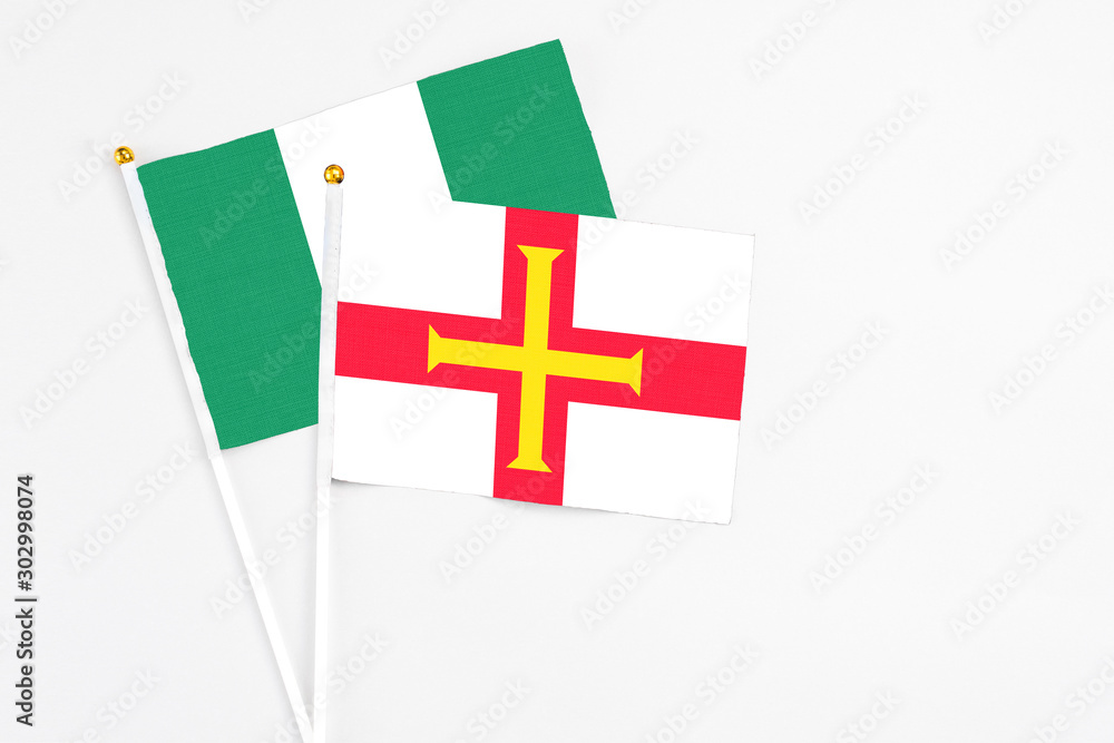 Guernsey and Nigeria stick flags on white background. High quality fabric, miniature national flag. Peaceful global concept.White floor for copy space.