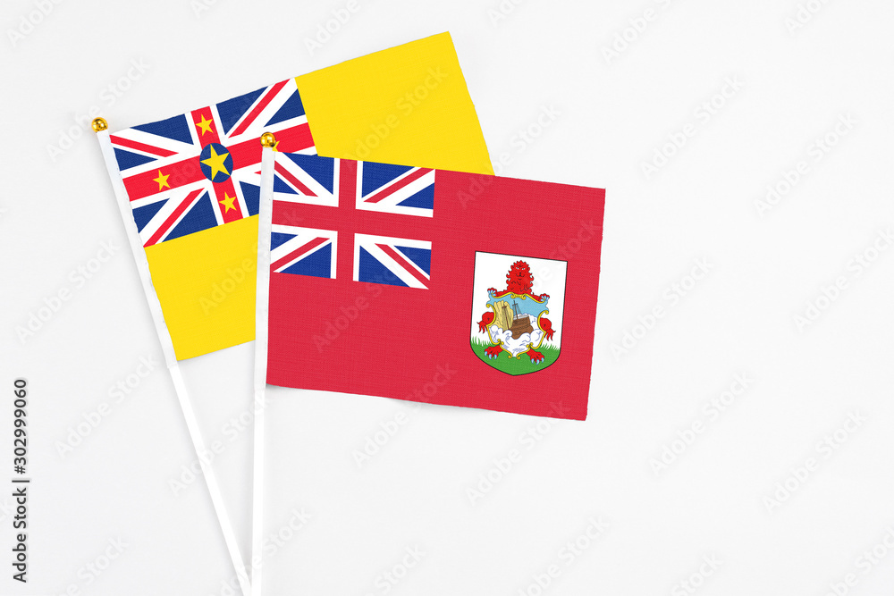 Fototapeta premium Bermuda and Niue stick flags on white background. High quality fabric, miniature national flag. Peaceful global concept.White floor for copy space.
