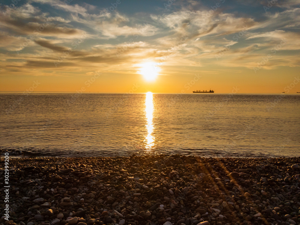 The bright autumn sun is reflected in the water of the sea with ships on the horizon against the blue cloudy sky at sunset in the evening. The bright autumn sun is reflected in the water of the sea with ships on the horizon against the blue cloudy sky at sunset in the evening.