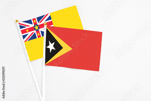 East Timor and Niue stick flags on white background. High quality fabric, miniature national flag. Peaceful global concept.White floor for copy space.
