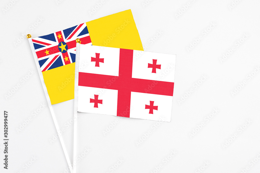 Georgia and Niue stick flags on white background. High quality fabric, miniature national flag. Peaceful global concept.White floor for copy space.