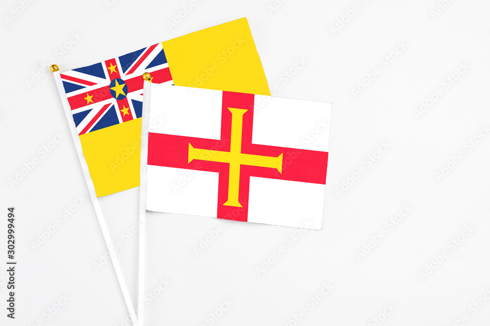 Guernsey and Niue stick flags on white background. High quality fabric, miniature national flag. Peaceful global concept.White floor for copy space.