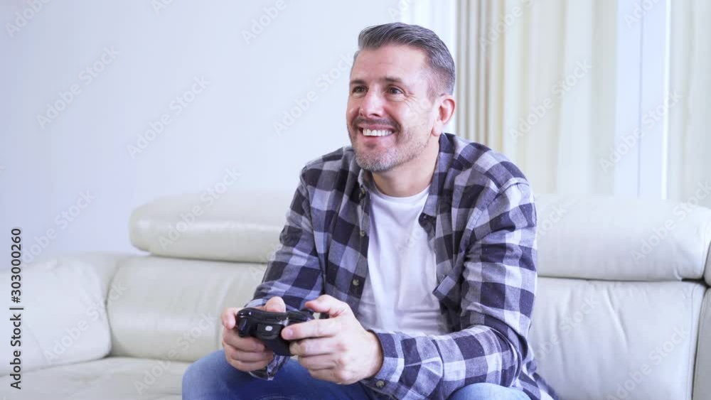 Handsome European man playing video games while sitting on the sofa in the living room at home. Shot in 4k resolution Handsome European man playing video games while sitting on the sofa in the living room at home. Shot in 4k resolution