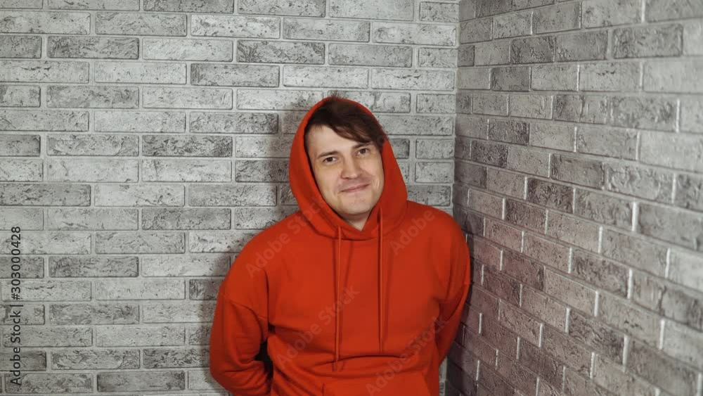 A beautiful emotional man in a red hoodie is happily surprised with hands on her cheeks. A beautiful emotional man in a red hoodie is happily surprised with hands on her cheeks.