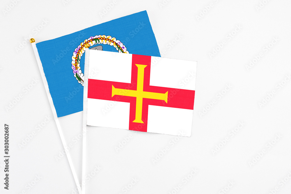 Guernsey and Northern Mariana Islands stick flags on white background. High quality fabric, miniature national flag. Peaceful global concept.White floor for copy space.