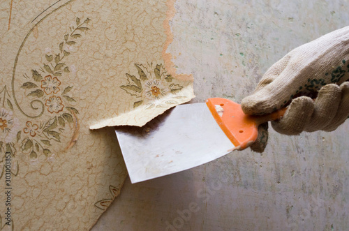 Preparing the wall for painting or sticking new wallpaper. Man in gloves with a scraper in the process of removing old wallpaper. wetted with a special solution surface