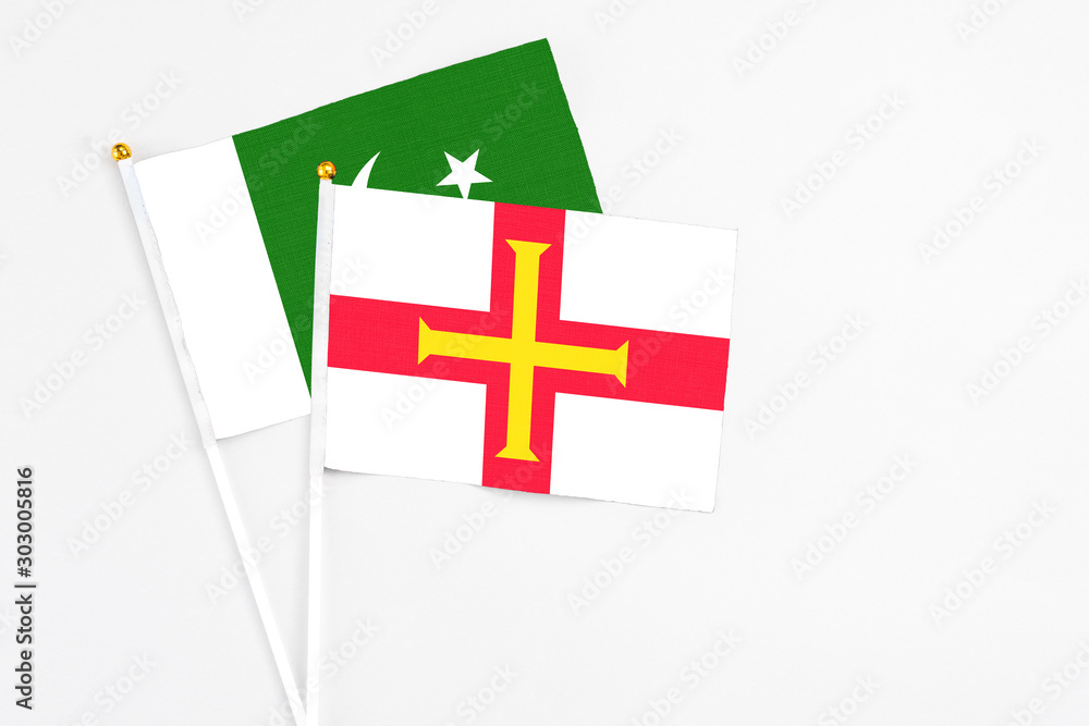 Guernsey and Pakistan stick flags on white background. High quality fabric, miniature national flag. Peaceful global concept.White floor for copy space.