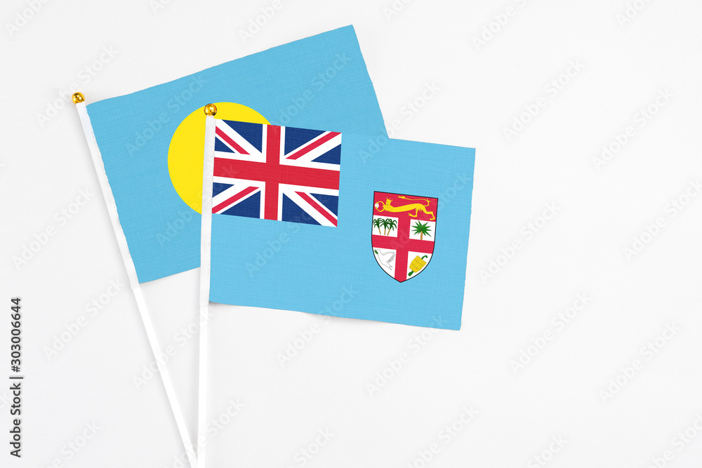 Fototapeta premium Fiji and Palau stick flags on white background. High quality fabric, miniature national flag. Peaceful global concept.White floor for copy space.