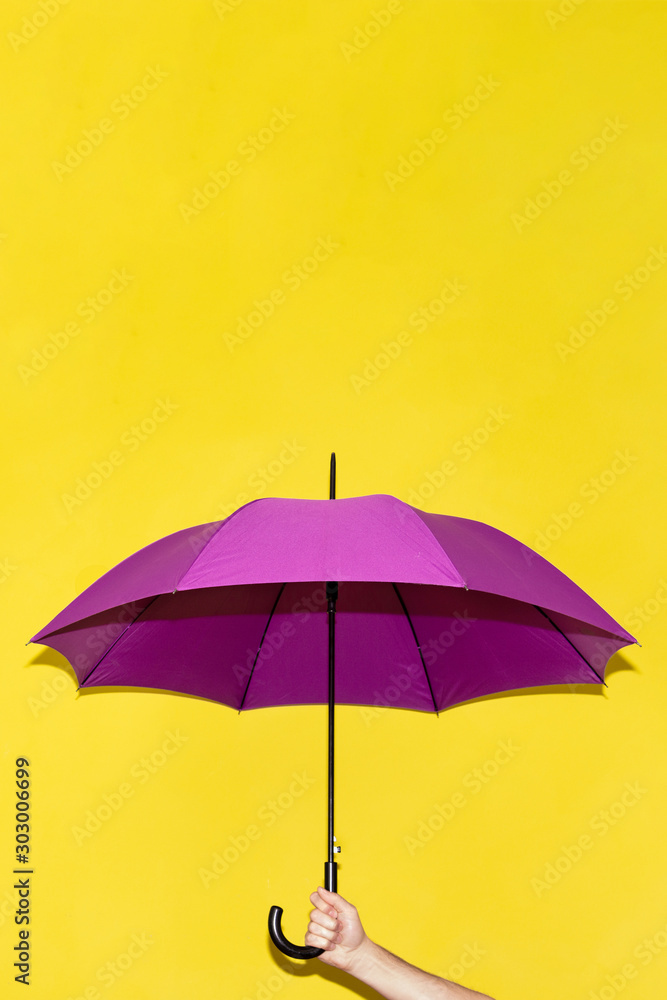 A man holds in his hand a purple umbrella on a background of yellow lime wall. Concept autumn, business, art.