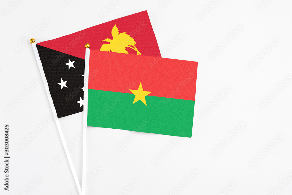 Burkina Faso and Papua New Guinea stick flags on white background. High quality fabric, miniature national flag. Peaceful global concept.White floor for copy space.