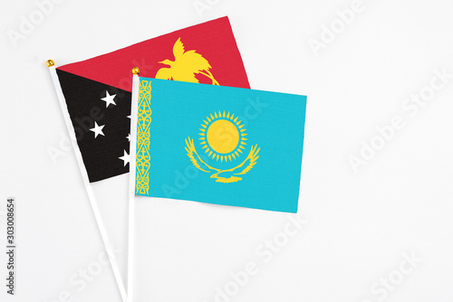 Kazakhstan and Papua New Guinea stick flags on white background. High quality fabric, miniature national flag. Peaceful global concept.White floor for copy space.