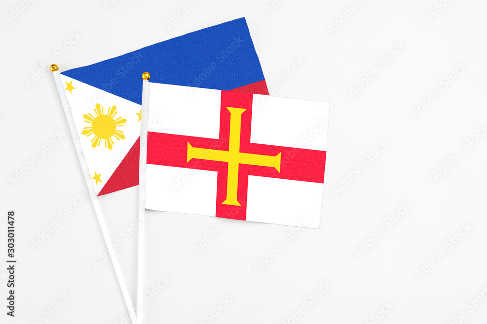 Guernsey and Philippines stick flags on white background. High quality fabric, miniature national flag. Peaceful global concept.White floor for copy space.