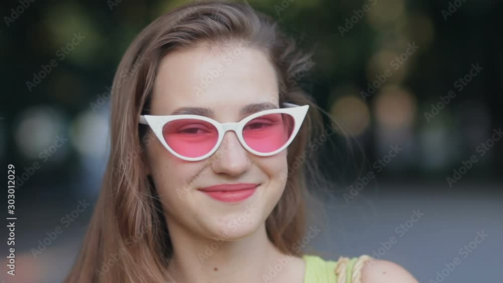 Pretty girl looking at camera and smiling wearing pink sunglasses Pretty girl looking at camera and smiling wearing pink sunglasses