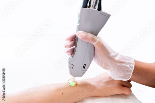 Close up of arm laser hair removal session with beauty technician and female patient, epilating after shaving, in a cosmetology skin clinic.