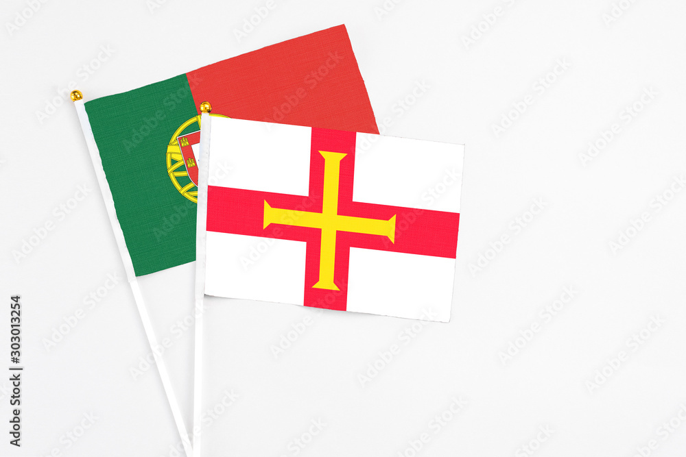 Guernsey and Portugal stick flags on white background. High quality fabric, miniature national flag. Peaceful global concept.White floor for copy space.