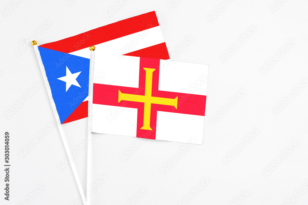 Guernsey and Puerto Rico stick flags on white background. High quality fabric, miniature national flag. Peaceful global concept.White floor for copy space.