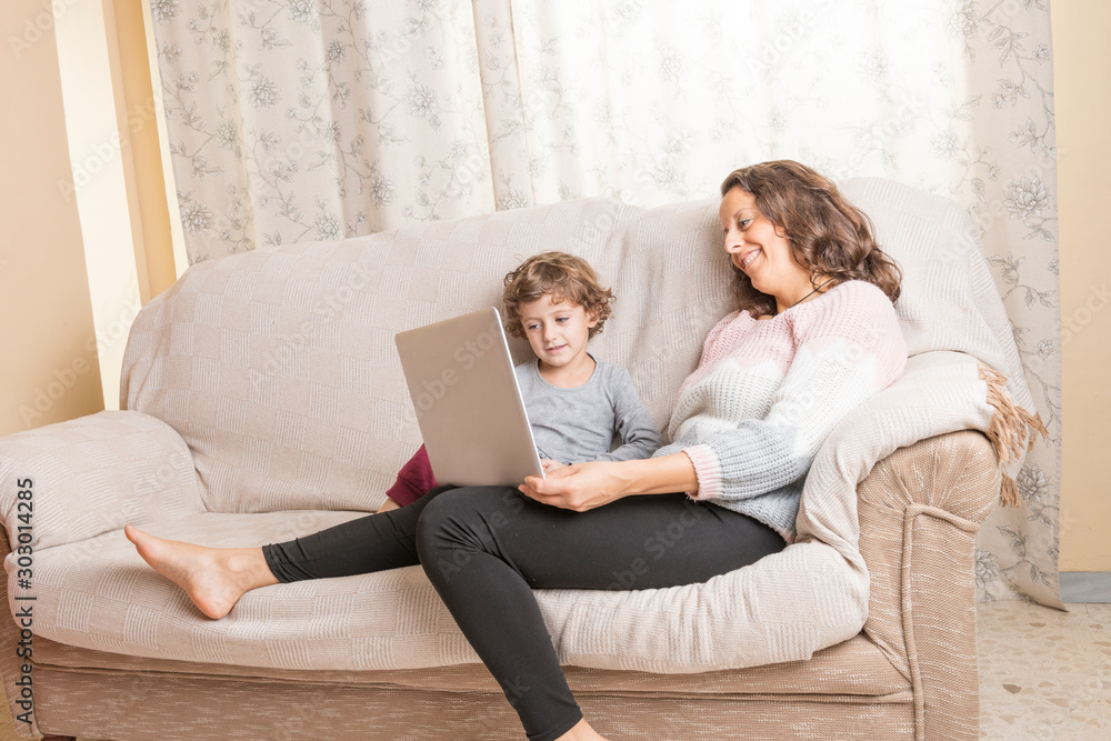Child and woman sitting on a sofa watching a laptop.