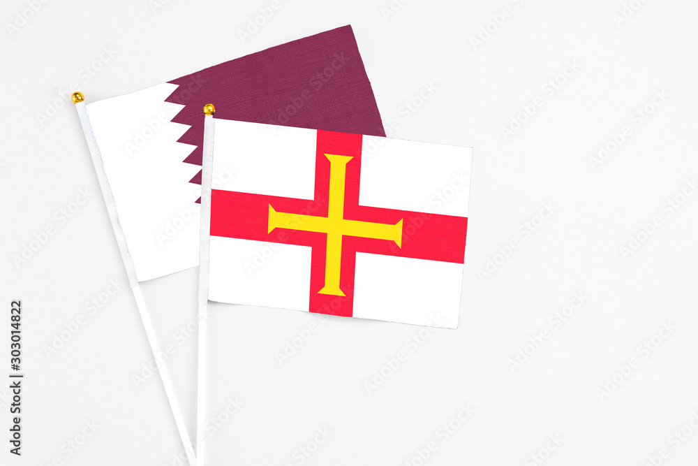 Guernsey and Qatar stick flags on white background. High quality fabric, miniature national flag. Peaceful global concept.White floor for copy space.